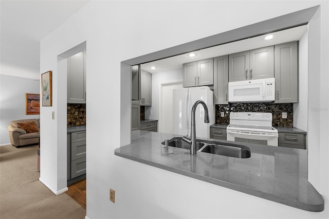 kitchen with kitchen peninsula, white appliances, backsplash, and sink