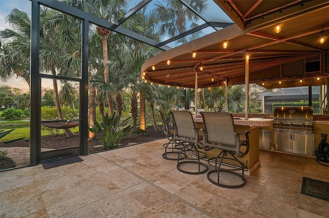 patio terrace at dusk with a bar, an outdoor kitchen, and area for grilling