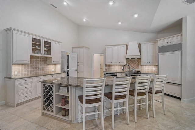 kitchen featuring premium range hood, white cabinets, a center island with sink, and high vaulted ceiling