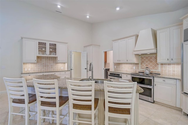 kitchen with a kitchen island with sink, appliances with stainless steel finishes, a breakfast bar area, custom range hood, and white cabinets