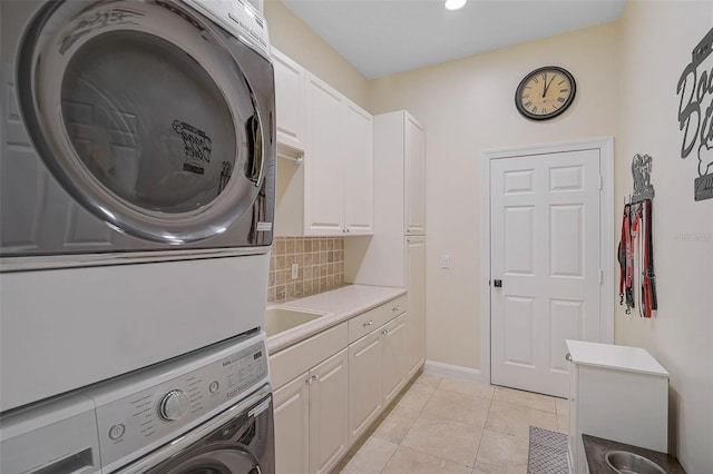 clothes washing area with cabinets, stacked washer / dryer, and light tile patterned flooring