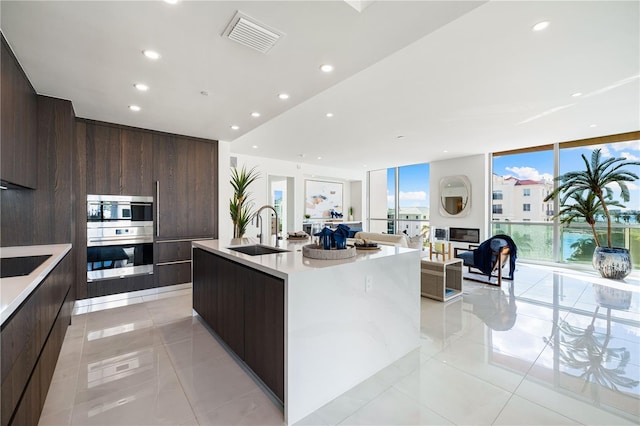 kitchen featuring sink, a wall of windows, black electric stovetop, an island with sink, and light tile patterned flooring