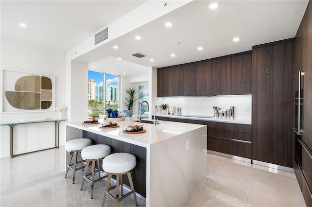 kitchen featuring wooden walls, sink, a kitchen breakfast bar, a kitchen island with sink, and dark brown cabinets