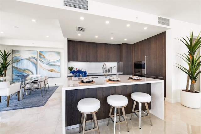 kitchen with double oven, dark brown cabinets, a kitchen breakfast bar, and a center island with sink