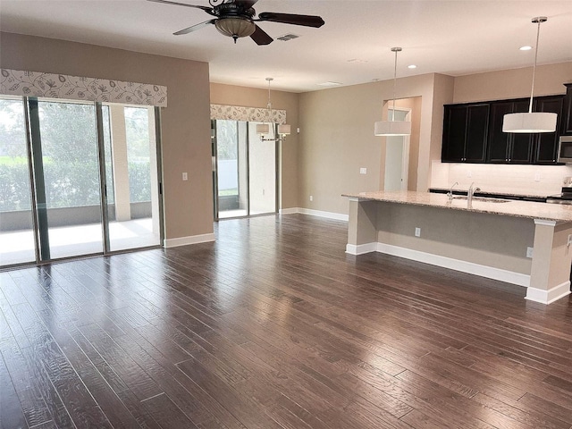 kitchen with light stone countertops, a breakfast bar, hanging light fixtures, and ceiling fan with notable chandelier