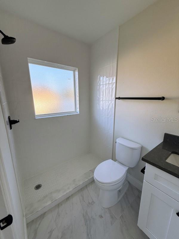 bathroom with tiled shower, vanity, toilet, and a wealth of natural light