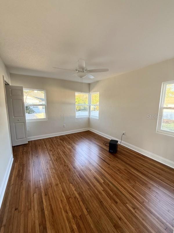 unfurnished room featuring a healthy amount of sunlight, ceiling fan, and dark wood-type flooring