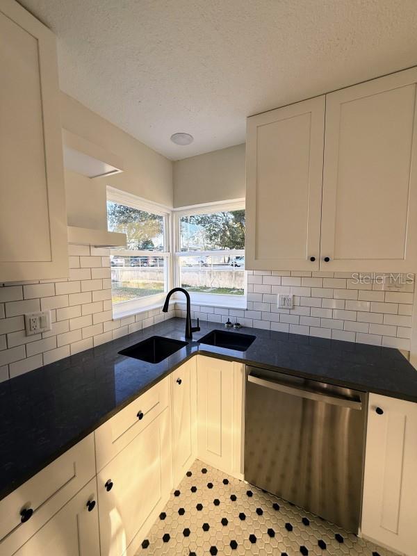 kitchen featuring tasteful backsplash, sink, white cabinets, and stainless steel dishwasher