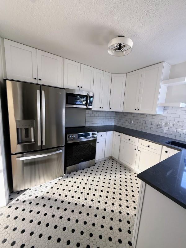 kitchen with tasteful backsplash, white cabinets, a textured ceiling, and appliances with stainless steel finishes