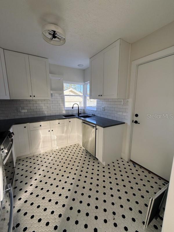 kitchen with decorative backsplash, stainless steel dishwasher, sink, range, and white cabinetry