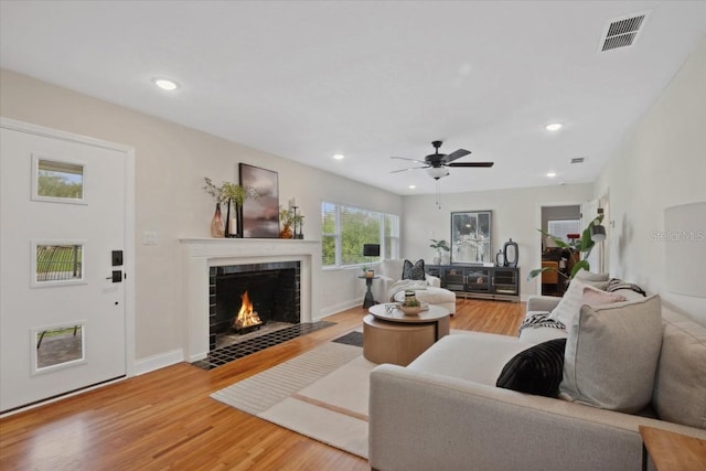 living room featuring ceiling fan, a tiled fireplace, and hardwood / wood-style floors