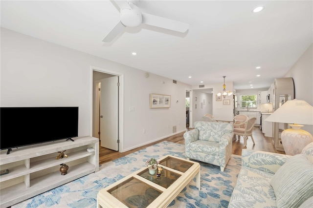 living room featuring ceiling fan with notable chandelier and light wood-type flooring