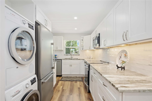 kitchen with light wood-type flooring, stainless steel appliances, sink, stacked washer and clothes dryer, and white cabinetry