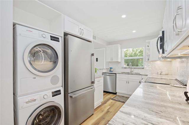 kitchen featuring light stone countertops, stainless steel appliances, sink, stacked washer and clothes dryer, and white cabinetry