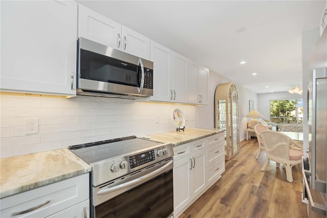 kitchen with light stone counters, white cabinetry, stainless steel appliances, and light hardwood / wood-style flooring