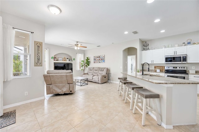 kitchen with a kitchen bar, light stone counters, stainless steel appliances, sink, and white cabinets