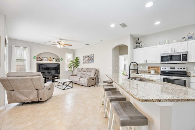 kitchen featuring white cabinetry, sink, stainless steel appliances, light stone counters, and a breakfast bar area