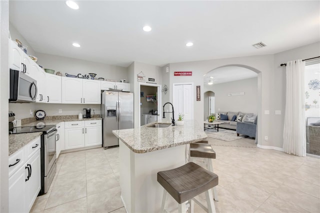 kitchen with sink, stainless steel appliances, light stone counters, an island with sink, and white cabinets