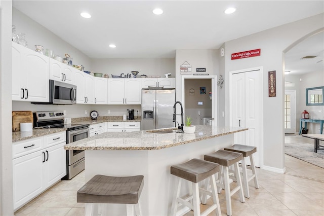 kitchen featuring white cabinets, a breakfast bar, an island with sink, and appliances with stainless steel finishes