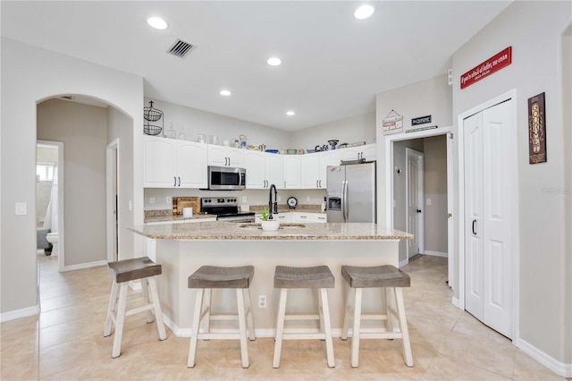 kitchen featuring light stone countertops, appliances with stainless steel finishes, white cabinetry, and a breakfast bar area