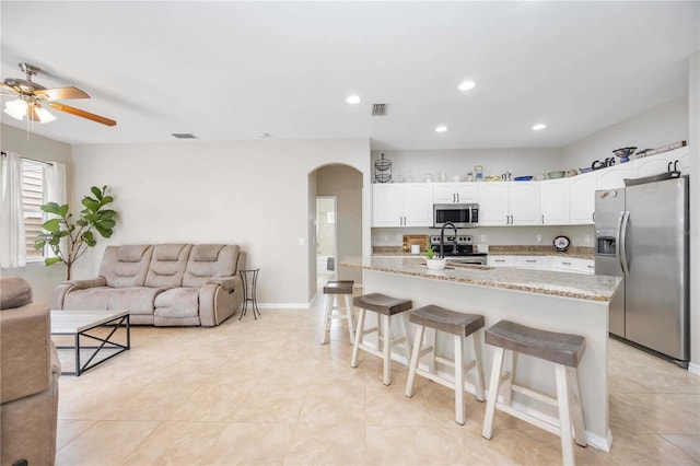 kitchen featuring white cabinetry, ceiling fan, stainless steel appliances, light stone counters, and a breakfast bar area