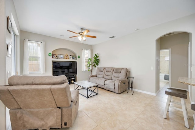 tiled living room with ceiling fan, plenty of natural light, and built in shelves