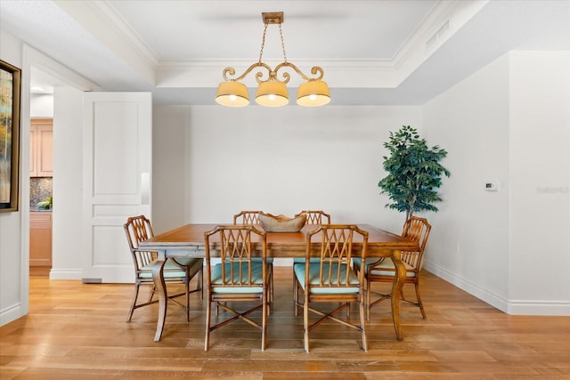 dining room with a raised ceiling, wood-type flooring, crown molding, and an inviting chandelier