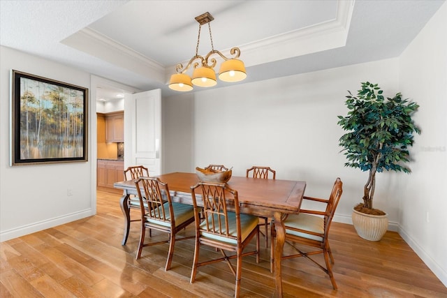 dining room with a raised ceiling, ornamental molding, light hardwood / wood-style floors, and an inviting chandelier