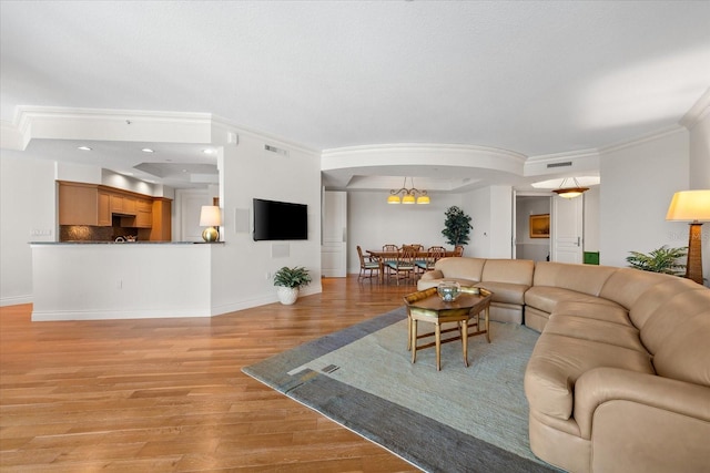 living room with an inviting chandelier, ornamental molding, and light hardwood / wood-style flooring