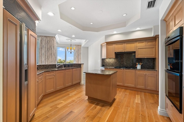 kitchen with black appliances, a kitchen island, a raised ceiling, and light wood-type flooring