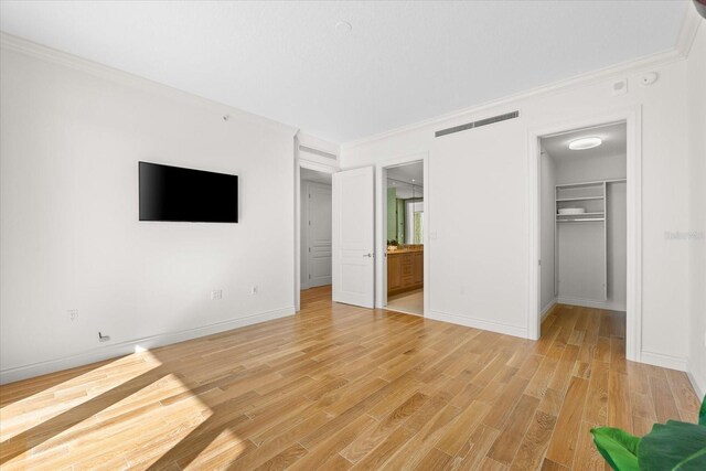 unfurnished bedroom with ensuite bath, light wood-type flooring, a spacious closet, ornamental molding, and a closet