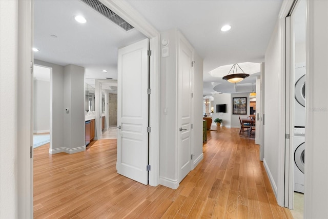 hallway with light hardwood / wood-style floors and stacked washer / drying machine