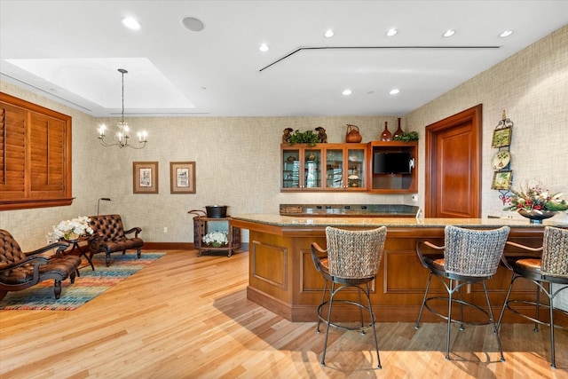 bar with pendant lighting, a tray ceiling, light hardwood / wood-style flooring, and a notable chandelier