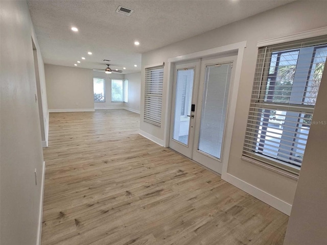 empty room with french doors, a textured ceiling, light hardwood / wood-style floors, and ceiling fan