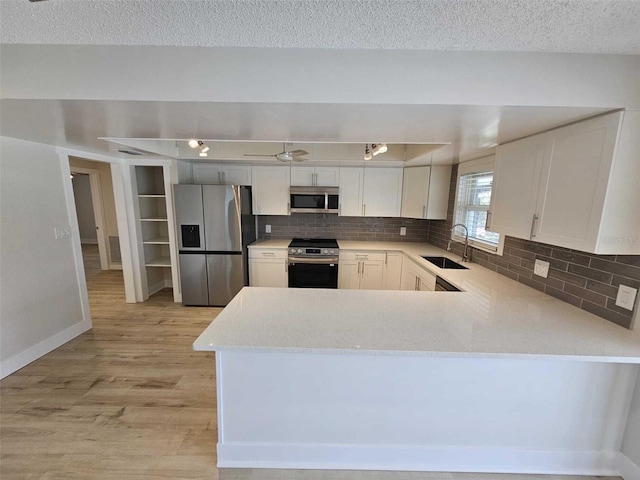 kitchen featuring kitchen peninsula, appliances with stainless steel finishes, tasteful backsplash, sink, and white cabinets