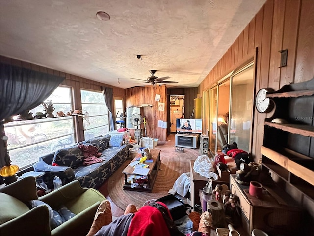 living room with a textured ceiling, wood walls, and ceiling fan