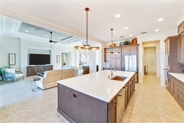 kitchen featuring appliances with stainless steel finishes, hanging light fixtures, an island with sink, a tray ceiling, and sink