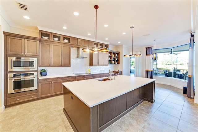 kitchen with appliances with stainless steel finishes, an island with sink, pendant lighting, wall chimney exhaust hood, and sink