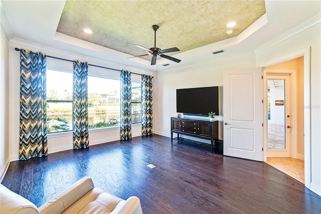 unfurnished living room featuring a raised ceiling, ceiling fan, crown molding, and dark hardwood / wood-style flooring