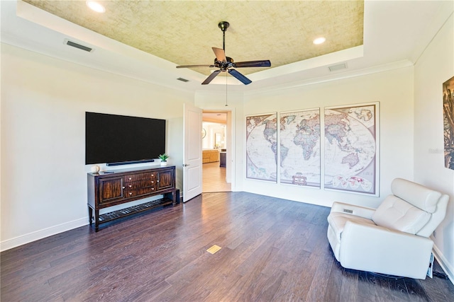 living area with dark wood-type flooring, a raised ceiling, ceiling fan, and ornamental molding