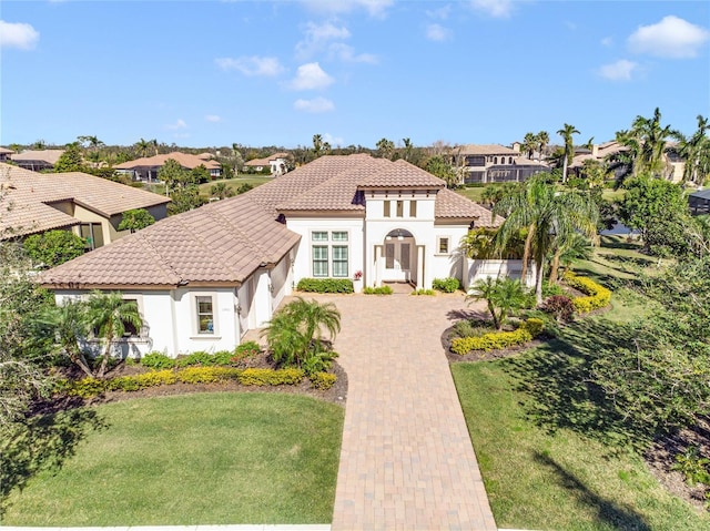 mediterranean / spanish-style house with decorative driveway, a tile roof, stucco siding, a front yard, and a residential view