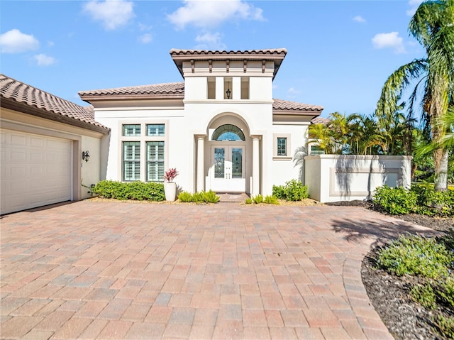 mediterranean / spanish-style house featuring an attached garage, stucco siding, a tile roof, and french doors