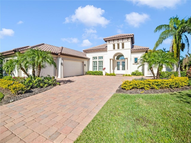 mediterranean / spanish home with decorative driveway, french doors, stucco siding, an attached garage, and a tiled roof