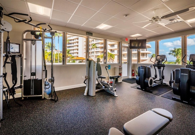 exercise room with a ceiling fan, a paneled ceiling, plenty of natural light, and baseboards