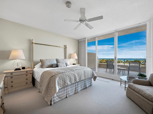 bedroom featuring a textured ceiling, light colored carpet, a ceiling fan, access to outside, and a wall of windows