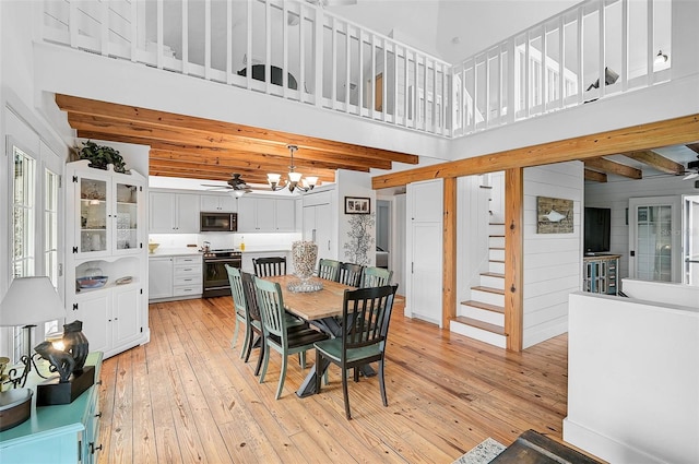 dining space featuring ceiling fan with notable chandelier, a high ceiling, light hardwood / wood-style flooring, and beamed ceiling