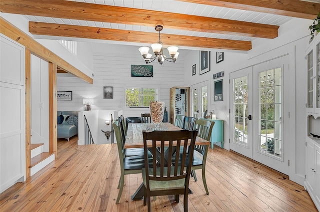 dining room with a notable chandelier, beam ceiling, a wealth of natural light, wooden walls, and french doors