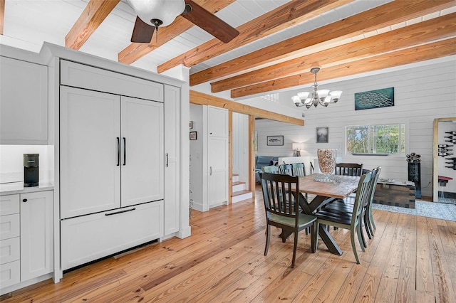 dining space with wood walls, light hardwood / wood-style floors, beam ceiling, and ceiling fan with notable chandelier