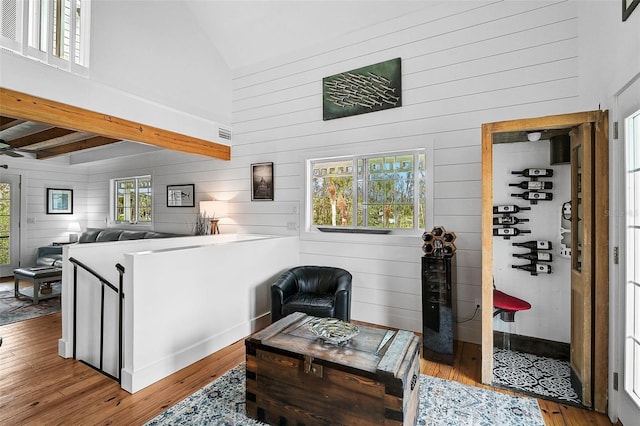 living room featuring beam ceiling, wood-type flooring, wooden walls, and high vaulted ceiling