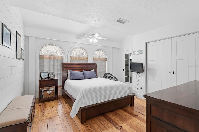 bedroom featuring a textured ceiling, light wood-type flooring, a closet, vaulted ceiling, and ceiling fan